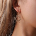 Orecchini dorati a forma di sole geometrico indossati da una modella in vista laterale - Stile Gancio Bohemien Sole Dorato (10073)