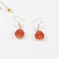 Dettaglio di orecchini rotondi in resina arancione con bordo in metallo dorato su sfondo bianco - Arancione
