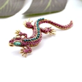 Goldene Gecko-Brosche mit lila und blauen Kristallen auf weißem Grund mit grünem Blatt - Rosarot