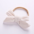 Detail of a handmade beige velvet bow on an elastic nylon headband for infants - White