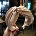 Detail of a champagne satin wide headband with a twisted knot design held by hand - Beige