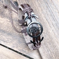 Dettaglio del bracciale in pelle intrecciata con chiave di violino su legno rustico - Marrone