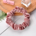 Pink velvet scrunchie with pleated texture on white card with decorative props - Pink