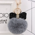 Detail of grey plush pom-pom keychain with leopard bow and gold hardware on a desk - Dark Gray