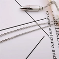 Gros plan d'un collier avec pendentif balle en argent et chaîne en métal sur fond clair - Pendentif Balle (Chaîne Croisée)