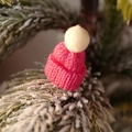 Mini pink and white knitted Christmas hat decoration placed on a snowy pine branch - Rose Red