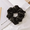 Detailed close-up of a premium black satin scrunchie with a silky texture on a white book - Black