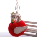Close-up of red swan pom-pom keychain with golden crown and wings on white bench - 8cm Fur Ball Gold Chain Buckle / Red