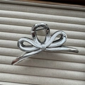 Close-up of silver metal bow hair claw clip displayed on a minimalist beige ribbed stand - Small Bowknot Silver 13cm