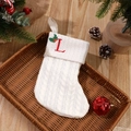 White knitted Christmas stocking featuring red embroidered letter L with holly in a basket - Letter L
