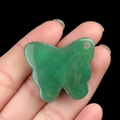 Green aventurine crystal butterfly pendant hand-held against a black background - Green Aventurine