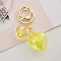 Détail macro de deux pendentifs cœur en résine jaune sur un porte-clés doré chic - Jaune Citron