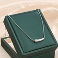 Detalle de un collar de acero de titanio plateado con colgante curvo minimalista en caja - Plateado