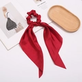 Dark red satin scrunchie with long ribbons and smooth silk texture on wood tray - Red