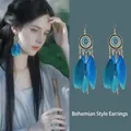 Detalle de pendientes bohemios de plumas azul pavo real con dijes de bronce en una modelo - 4# Estilo de Pluma Degradado Azul-Oro