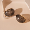 Dettaglio di orecchini vintage in resina con bordi dorati e trama a fumo nero - Nero