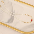 Dettaglio della collana di perline con ciondolo a pesce su vassoio in marmo bianco - Rosso