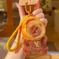 Cute Capybara plush keychain with orange hood and Bakery apron, hand-held in cafe - Lieba Bread Hat