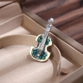 Close-up of a silver violin brooch with inlaid green gemstones in a beige gift box - Silver Base Green Rhinestone