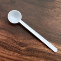 White plastic measuring spoon for milk powder on a dark rustic wooden surface - 1.5g (10.5*2.3*1cm) / White