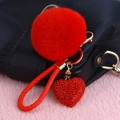 Detail of red rhinestone heart keychain with plush ball on a black leather handbag - Rhinestone Heart + Bright Red Pom