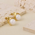 Close-up of golden pearl earrings with iridescent luster on a textured stone surface - Stud Earrings