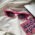 Detail shot of bright pink cat-eye sunglasses with dark lenses on a white textured background - Pointed Triangle