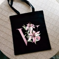 Black canvas tote bag with pink lily floral print and letter W on a neutral background - Letter W / Black