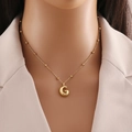 Golden bead chain necklace with polished letter G pendant worn on a female model - Letter G
