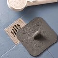 Dark grey square silicone drain cover with handle and water droplets on bathroom floor - Gray
