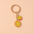 Detalle de un llavero dorado con dos rodajas de frutas realistas hechas de metal - Naranja