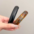 Classic spring hair clips in elegant black and tortoiseshell finish displayed in hand - Glossy Black + Blue Brown