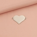 Vista de detalle de un colgante de corazón plateado con dos anillas sobre tela rosa - Color Acero