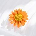 Macro shot of 3D orange daisy flower brooch with textured yellow center on white pedestal - Orange Daisy