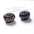 Macro-opname van twee kleine glow-in-the-dark Halloween pompoen kralen met gezichtje - Niet-lichtgevende zwarte pompoen oranje ogen / 3D