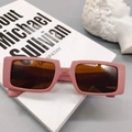 Detail view of pink rectangular sunglasses with brown lenses on a white book with a statue - Bean Paste Red