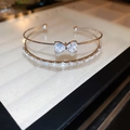 Detail of double-layer silver bangle featuring a zircon bow heart and tiered baguette crystals - Silver