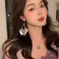 Detail of long heart crystal tassel earrings and blue butterfly necklace on model - Pearlescent Triangle Tassel (21# Ear Hook-White)