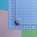 Macro shot of a 1.5cm purple resin plumeria flower accessory on a measurement grid mat - Purple