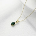 Collar de titanio dorado con un colgante de gema verde en forma de pera sobre tela blanca - Dorado + Circonita verde