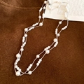 Dettaglio della collana lunga di perle multistrato con catena d'argento su sfondo materico - Bianco