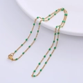 Detailed close-up of a golden O-chain necklace with green beads on a white ceramic plate - Gold - Green Beads