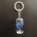 Detailed top view of miniature resin wine glass keychain with blue liquid on leather - Blue