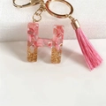 Close-up of resin letter H keychain with pink flakes, gold sequins and silk tassel - Letter H