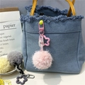 Close-up of colorful plush pom-pom charms with star clips on a blue denim bag - Pink