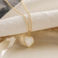 Close-up of golden heart pendant featuring elegant white marble texture inlay on soft fabric - White