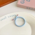 Light blue elastic hair tie with pink plastic end displayed on a white ceramic plate - Blue