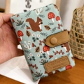 Light blue tri-fold fabric wallet featuring forest patterns and brown leather snap closure - Handheld Green Squirrel Pattern