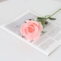 Lifelike single pink velvet rose artificial flower on a white table with magazine - Large Round Coral Pink