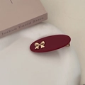 Macro view of burgundy oval hair clip with gold bow and metallic alligator clasp - Red